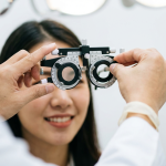 Optometrist adjusts a phoropter in front of a patient during an eye exam.